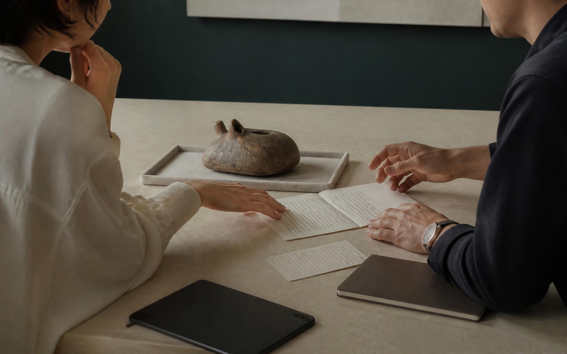 Consultor e especialista analisando um objeto colecionável e sua documentação sobre mesa de pedra clara